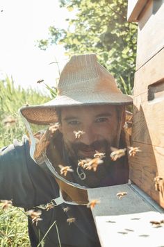 a man wearing a hat and holding a beehive in front of his face