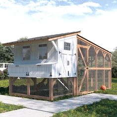 a white chicken coop sitting on top of a grass covered field next to a sidewalk