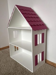 a white doll house with pink roof on carpeted floor