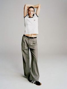 a woman in white shirt and grey pants posing for a photo with her hands behind her head