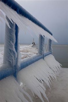 an ice - covered bench on the beach with a lighthouse in the background