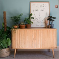 a wooden cabinet with plants on it in front of a painting and potted plants