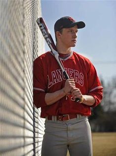 a man holding a baseball bat standing next to a fence