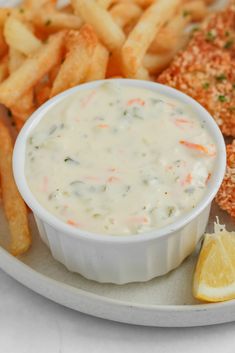 a white plate topped with fish and fries next to a bowl of dipping sauce on top of it