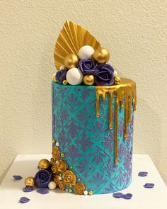 a blue and gold decorated cake with flowers on the top is sitting on a table