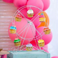 a ferris wheel with cupcakes on it in front of pink and orange balloons