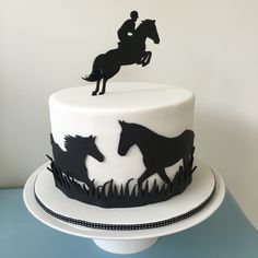 a white cake with black silhouettes of two horses and a rider on the top