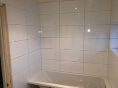 a bath tub sitting next to a window in a room with white tiles on the walls