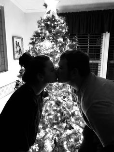 two people kissing in front of a christmas tree