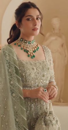 a woman wearing a green and gold outfit with jewelry on her neck, standing in front of a statue