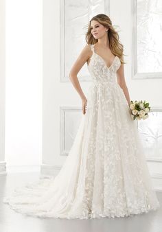 a woman in a wedding dress standing next to a white wall with flowers on it