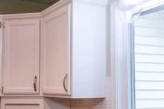 an empty kitchen with white cabinets and wood flooring in front of a sliding glass door