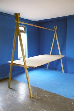 an empty room with blue walls and a wooden swing frame in the middle, next to a window