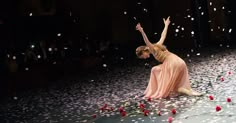 a woman sitting on the ground surrounded by flowers and petals with her arms in the air