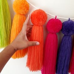 a hand is pointing at some tassels hanging from a string