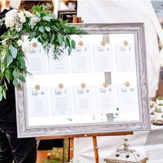 an easel with seating cards and greenery on it