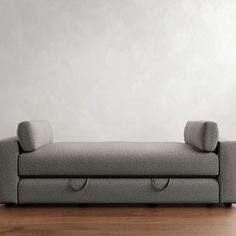 a gray couch sitting on top of a wooden floor next to a white wall in an empty room