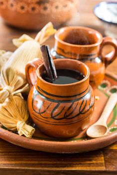 a plate topped with two mugs filled with liquid next to spices and spoons