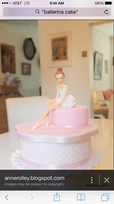 a pink cake with a woman sitting on top of it, in front of a dining room table