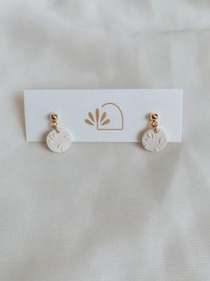 three pairs of earrings on top of a white card with gold accents and two small leaves