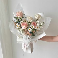 a person holding a bouquet of flowers in their hand with white and pink roses on it