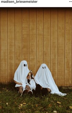 two people dressed as ghostes sitting in the grass