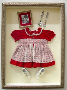 a shadow frame with a red dress and white shoes in front of a framed photo