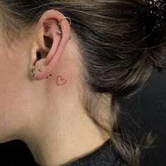 a woman with a tiny heart tattoo on her left side behind the ear, wearing a black top