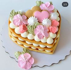 there is a heart shaped cake with flowers on the top and two cookies in the shape of hearts