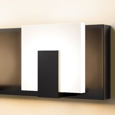 a black and white wall light mounted on the side of a wall next to a mirror