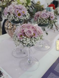 three wine glasses with flowers in them sitting on a table next to other vases