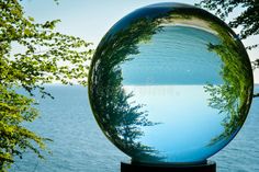 the reflection of trees in a glass ball on top of a black stand near water