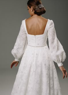 a woman in a white wedding dress with long sleeves and a backless neckline