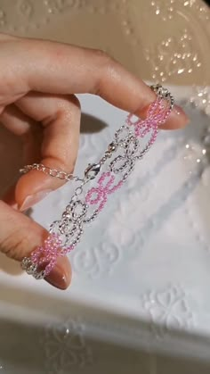 a woman's hand holding a chain with pink beads on it in front of a cake