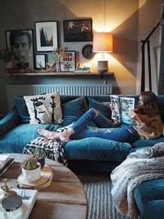 a woman sitting on top of a blue couch in a living room next to a lamp