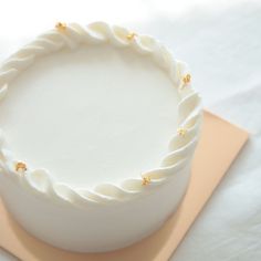 there is a white cake with gold decorations on the top and bottom, sitting on a pink plate