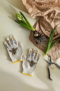 two white gloves sitting on top of a table next to some green plants and scissors