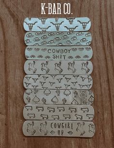 four metal tags with cowboy designs on them sitting on top of a wooden table next to a sign that says cowgirl up