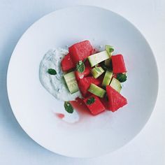 a white plate topped with watermelon, cucumber and yogurt