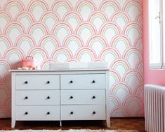 a baby's room with a dresser and wallpaper in pastel pinks