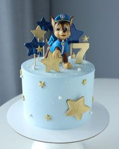 a blue cake with gold stars and a cartoon character on top is sitting on a white table