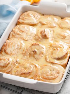 a white casserole dish filled with cinnamon rolls and oranges on a cooling rack