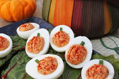 several deviled eggs are arranged on a leafy platter with pumpkins in the background