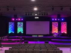 an empty auditorium with rows of seats and large screens on the wall, all lit up by brightly colored lights