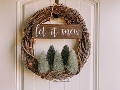 a wreath that says let it snow and three small pine trees are placed on the front door