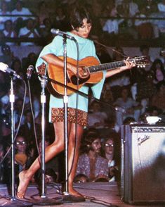 a woman standing in front of a microphone while holding a guitar