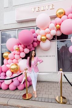 a woman standing in front of a pink and gold balloon arch on the side of a building