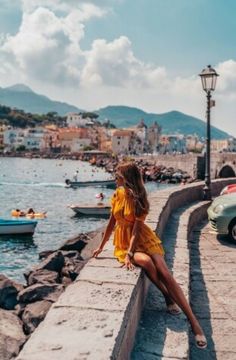 a woman sitting on the edge of a pier looking out at boats in the water