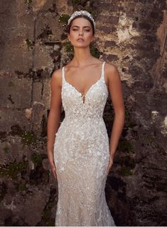 a woman in a wedding dress standing next to a stone wall with moss growing on it