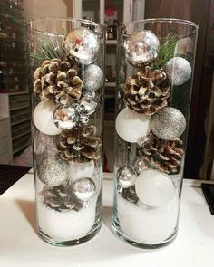 two clear vases with pine cones and balls in them sitting on a counter top